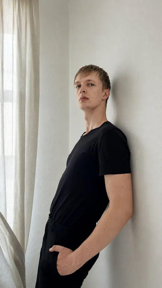 Editoriales Portrait von Lars Möllering an heller Wand, seitlich gelehnt, schwarzes Outfit, ruhige Distanz.